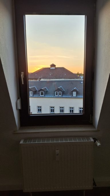 Blick aus einem Fenster auf ein Gebäude bei Sonnenuntergang.