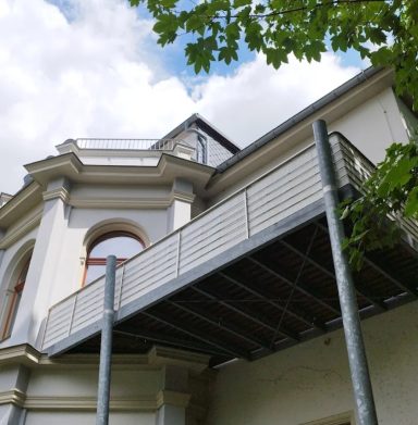 Balkon eines historischen Gebäudes mit grauem Geländer und vielen Fenstern.