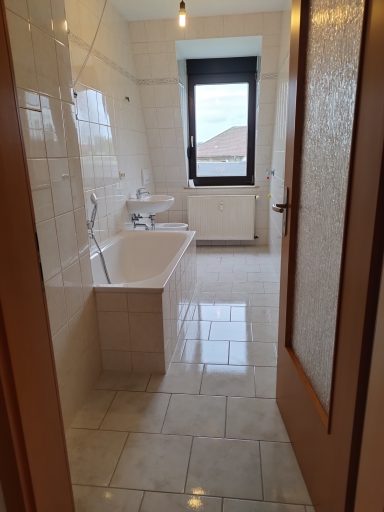 Helles Badezimmer mit Badewanne, Waschbecken und Fenster. Fliesenboden.