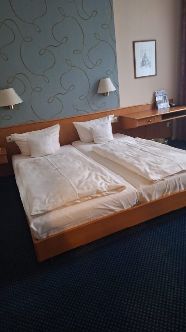 Zwei Einzelbetten mit weißen Bettdecken in einem hotelartigen Zimmer.