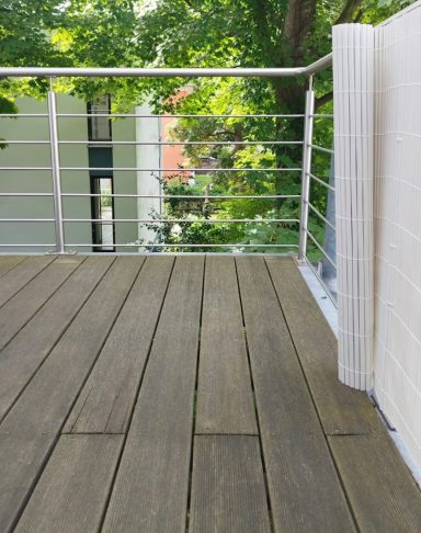 Holzterrasse mit Geländer und Blick auf Grünflächen im Hintergrund.