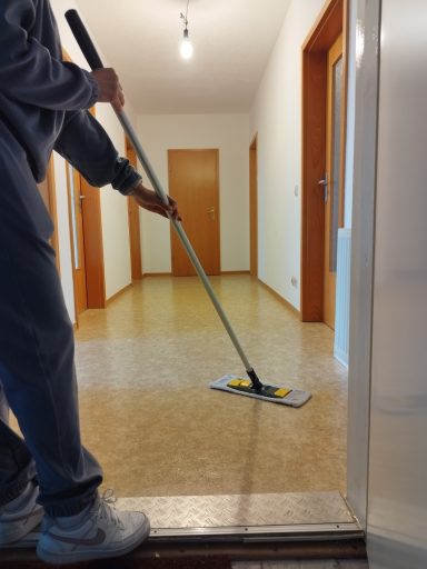 Person reinigt den Boden mit einem Wischmopp in einem hellen Raum.