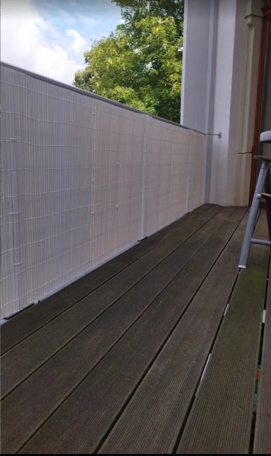 Holzterrasse mit Sicht auf einen begrünten Balkon und Himmel.