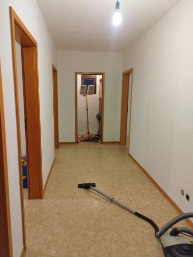 Ein leerer Flur mit hellen Wänden und einem Staubsauger auf dem Boden.