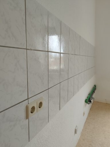 Weiß geflieste Wand mit Steckdosen und einem grünen Rohr darunter.